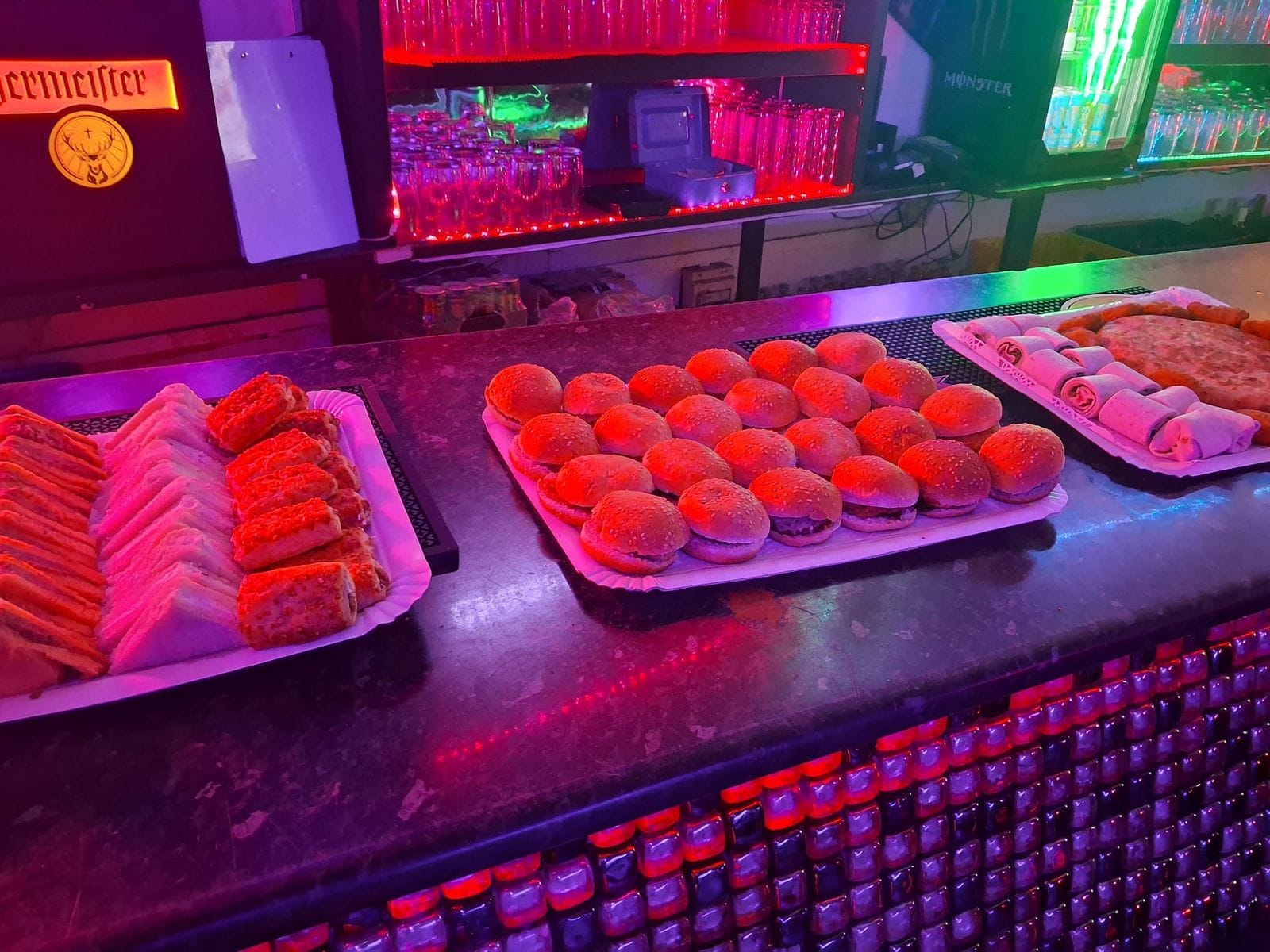 Bandejas de catering con minihamburguesas, sándwiches y rollitos servidas en la barra de TBC Huertas
